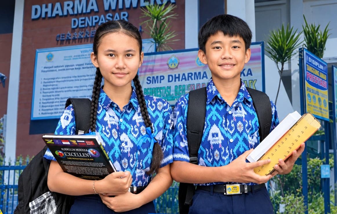 Dua siswa SMP Dharma Wiweka Denpasar berseragam di depan gedung sekolah